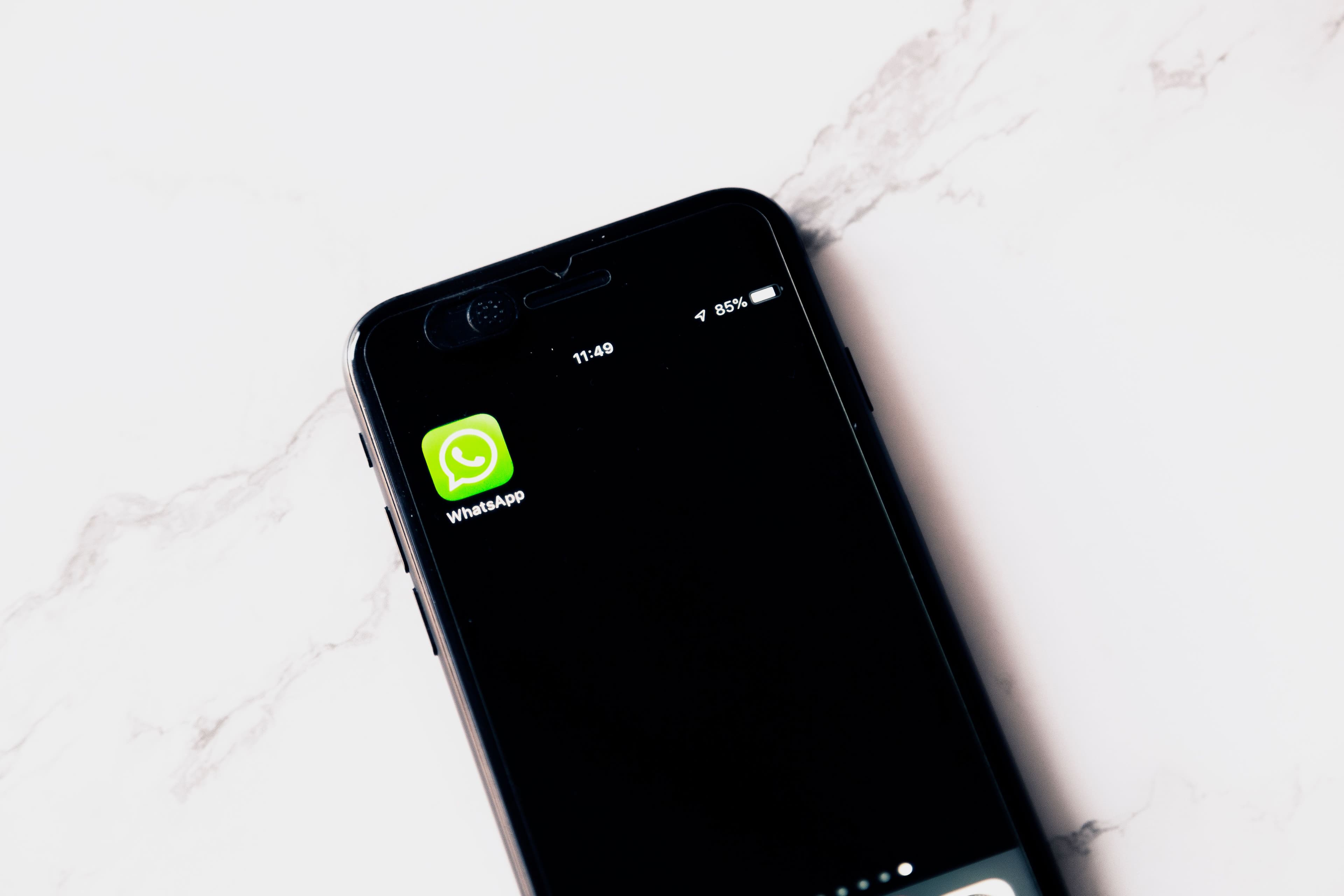 Close-up of a smartphone screen showing the WhatsApp app icon, resting on a marble-patterned table