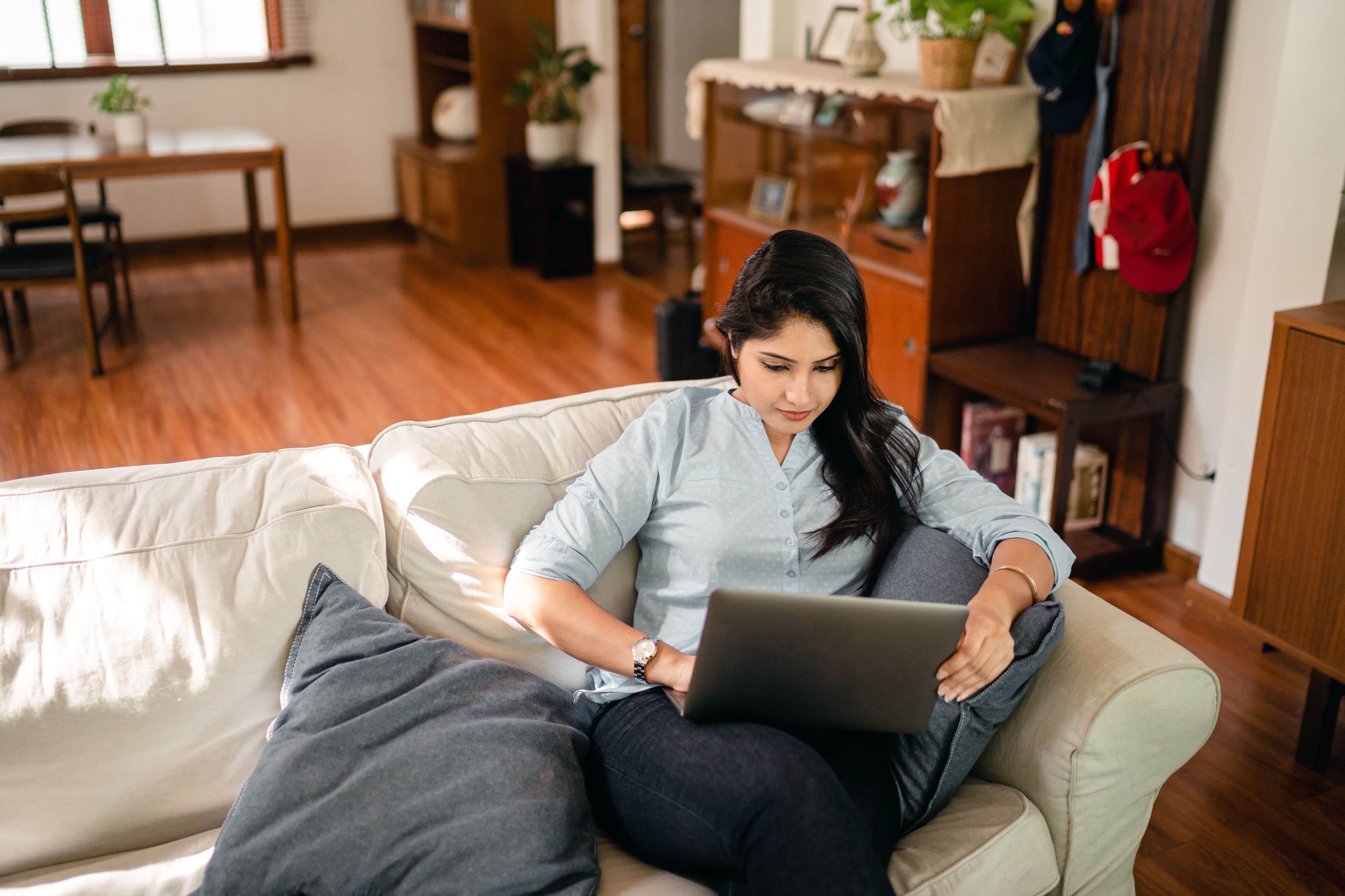 An overhead view of a young woman sitting on a sofa, typing on a laptop while working from home