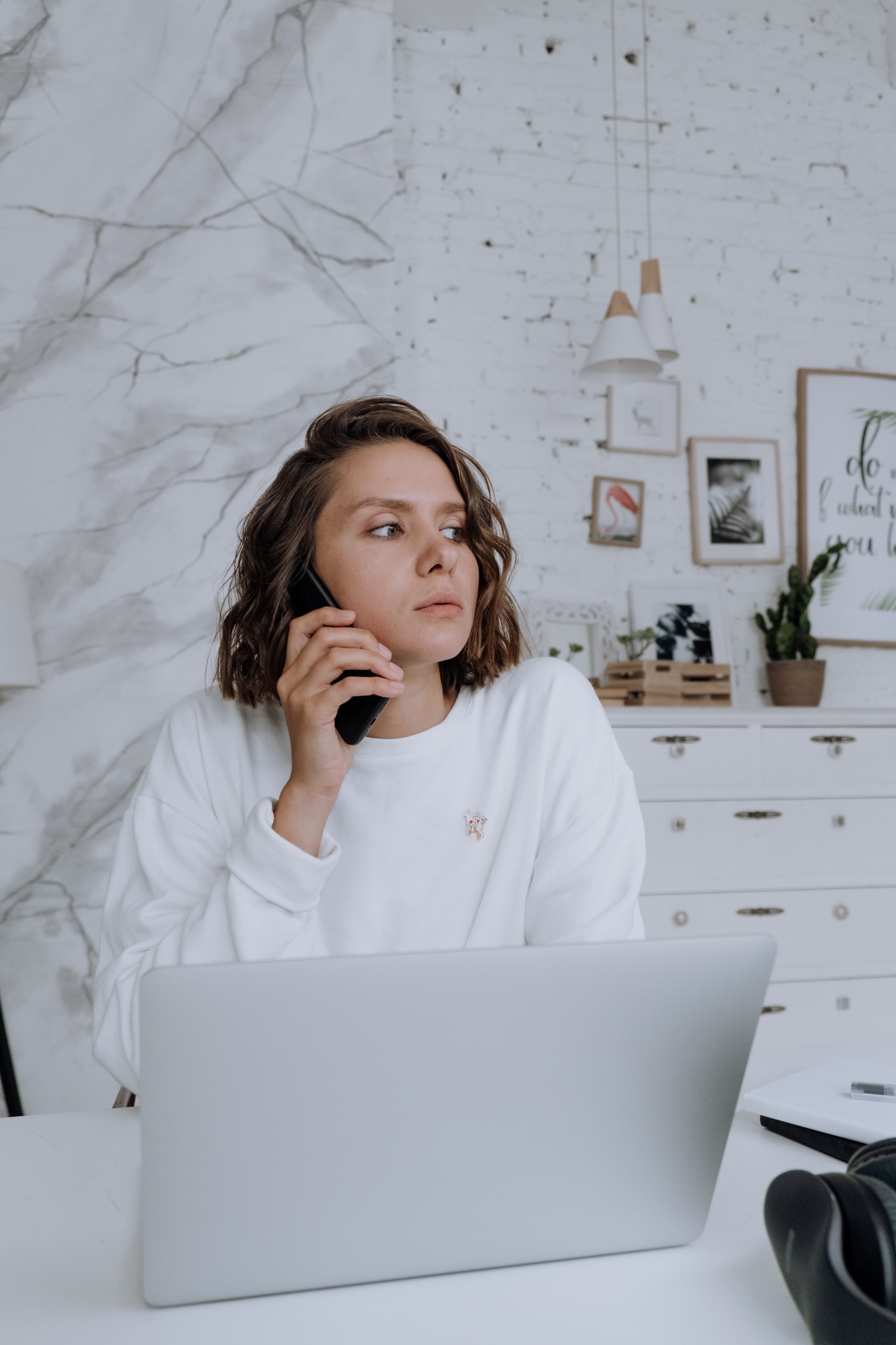 A businesswoman on a phone call at a minimalist home-office desk with a laptop open in front of her